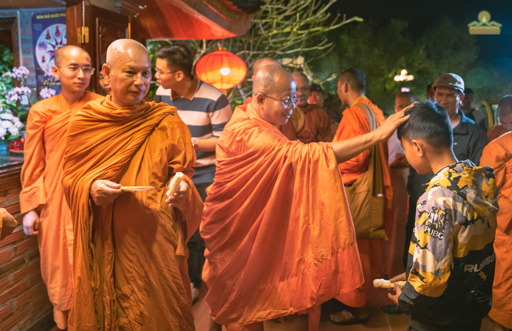 A venerable monk happily patted a childs head after giving a small dish to him.