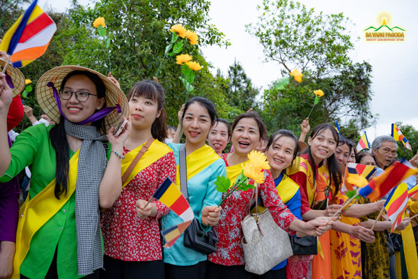 Female Buddhists in vibrant clothes waving flags and flowers to welcome the parade